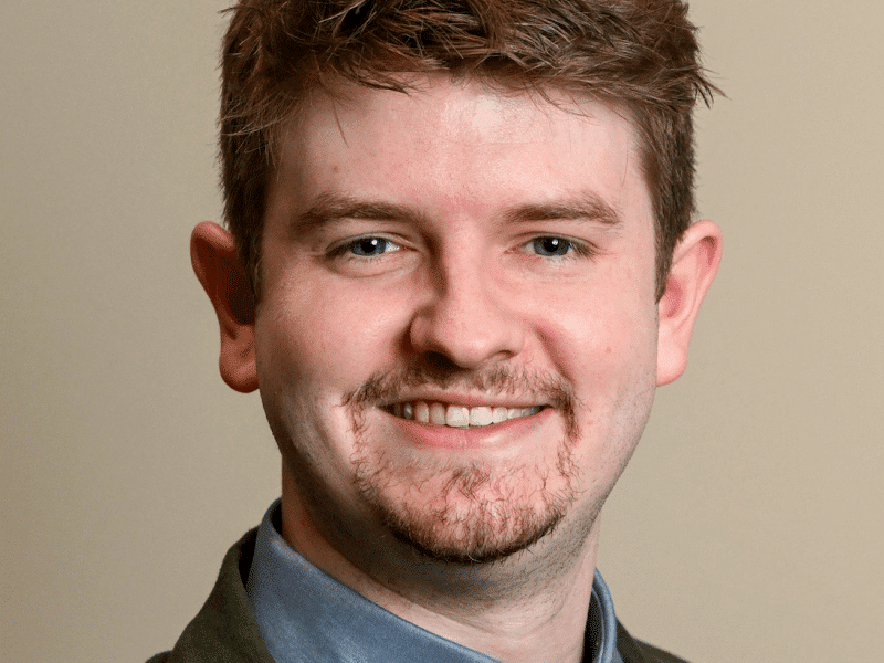 Micah Johnston poses for a standard headshot wearing a green jacket and tie.